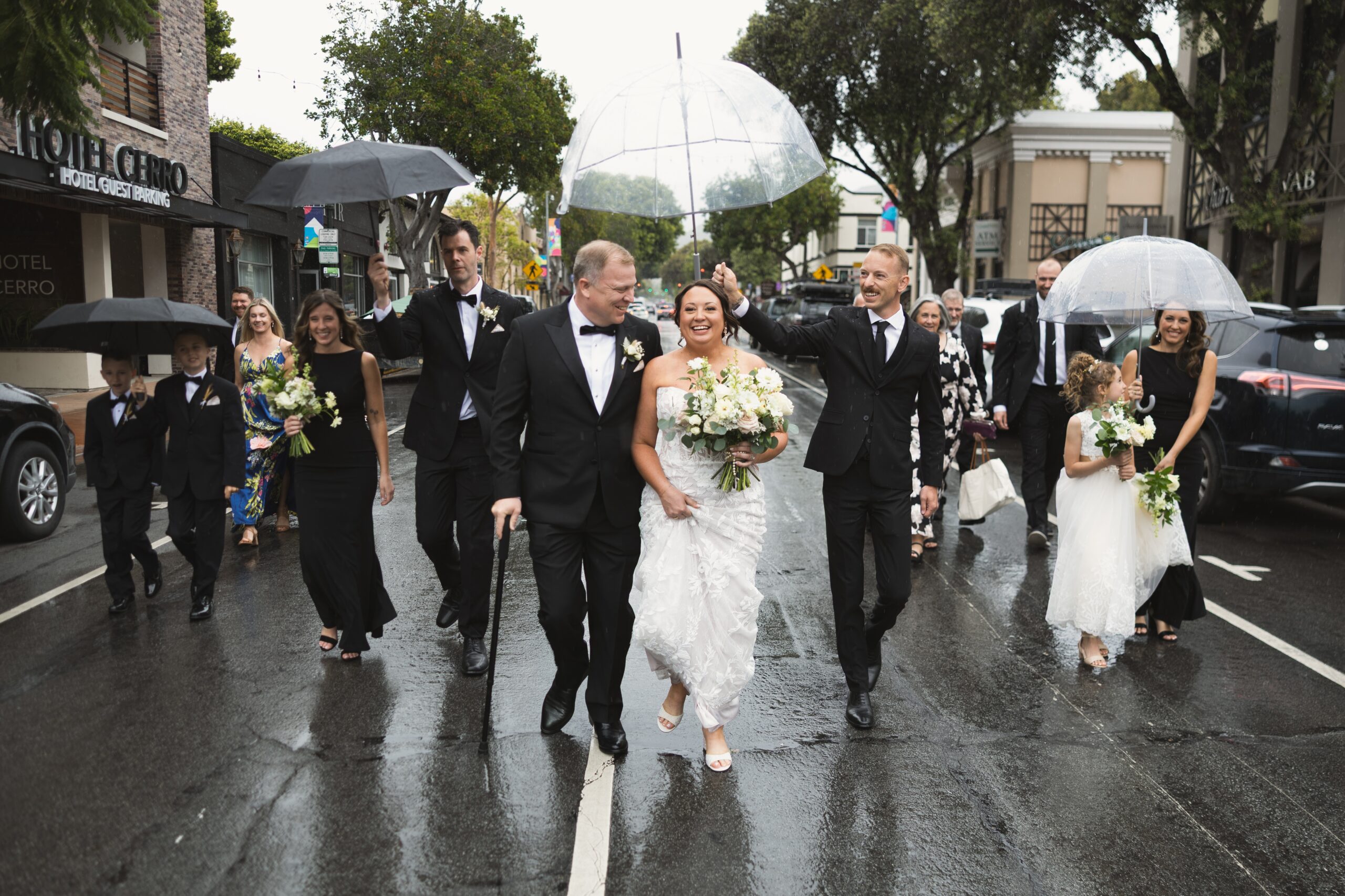 Bride and groom and their wedding party walking down the middle of a rain-soaked street in downtown San Luis Obispo during their wedding day portraits
