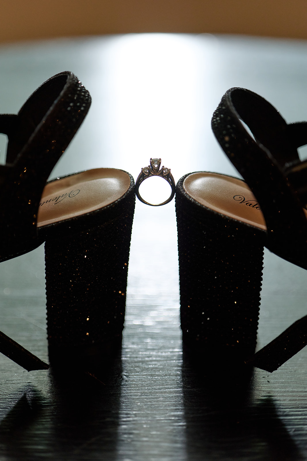 Engagement ring balanced between black glitter platform heels, backlit