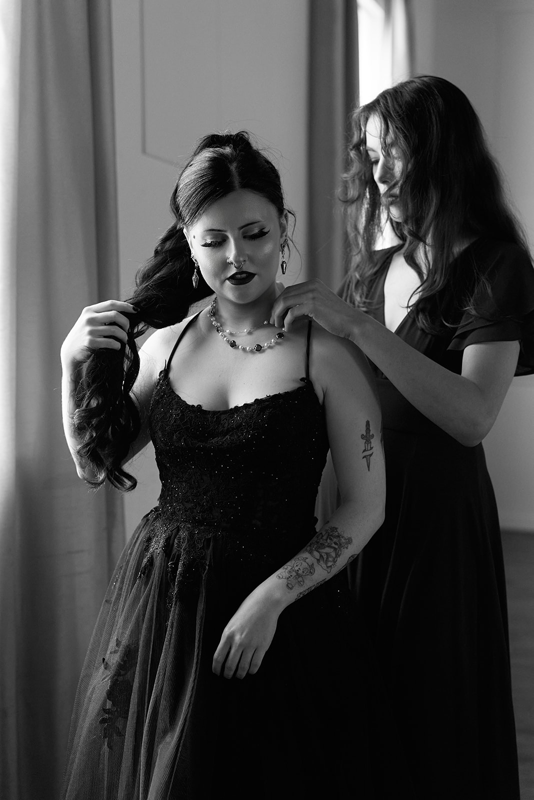 Black and white portrait of the bride's necklace being fastened by the window