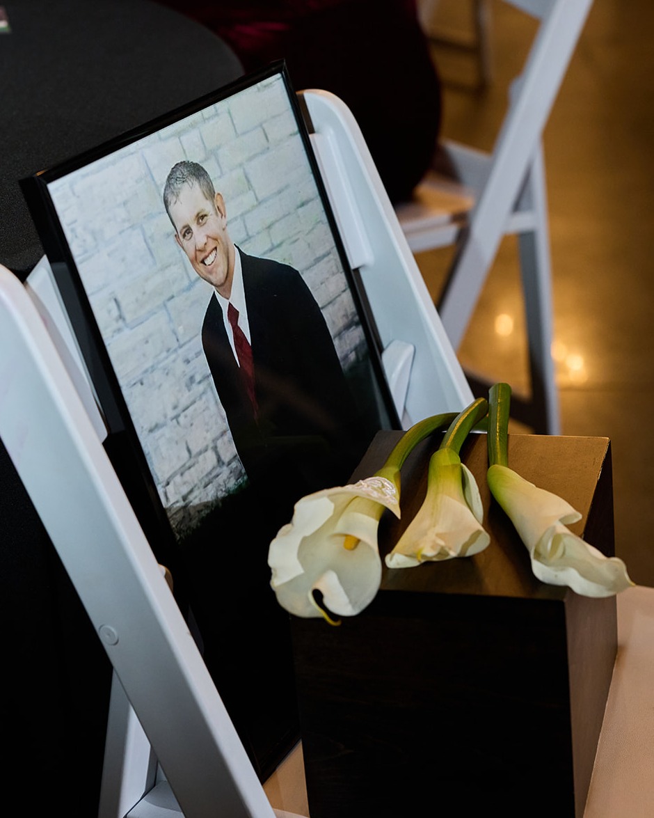 Framed photo of the bride's late father on a front row seat with white calla lilies and his urn