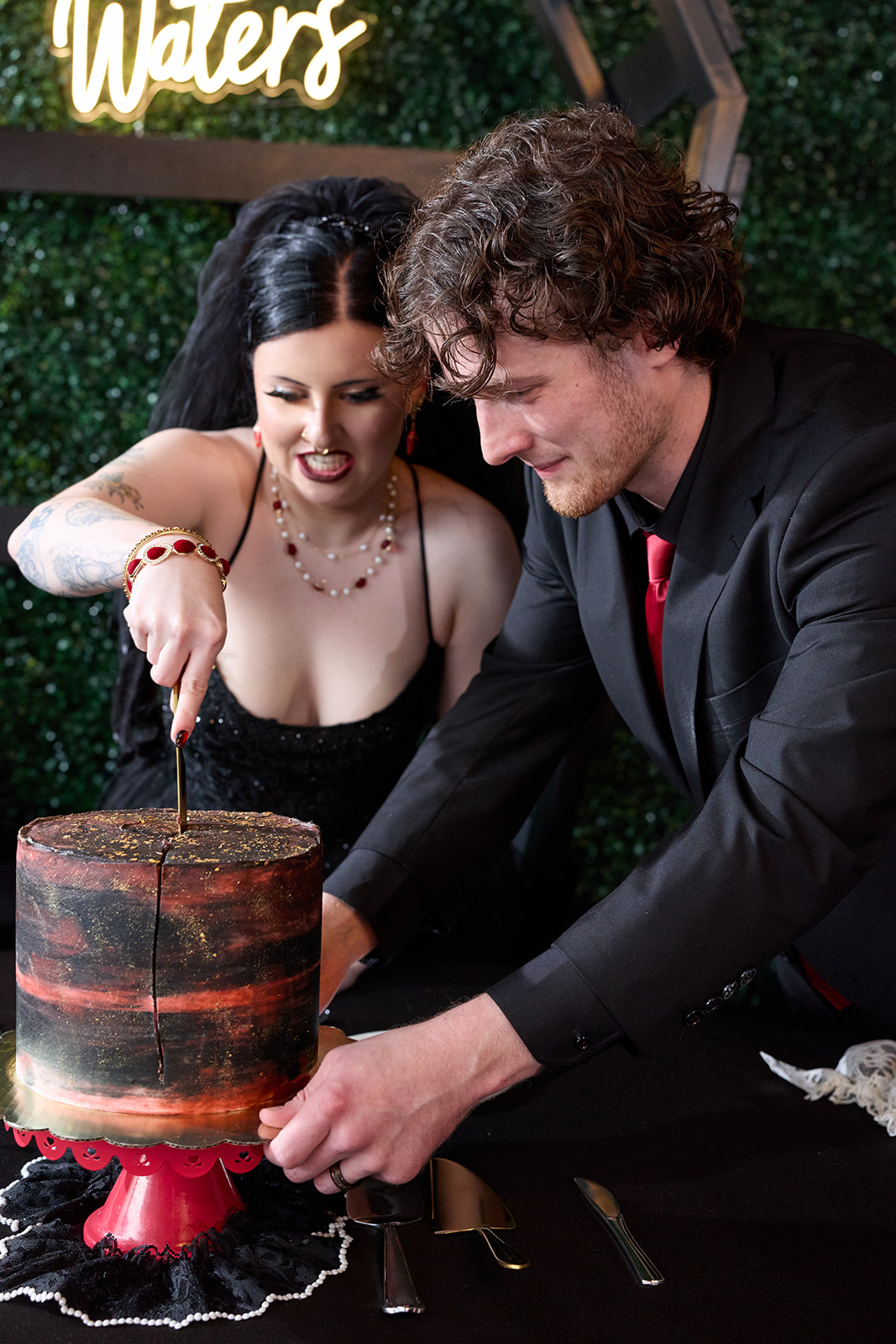 Bride and groom cutting a black and red wedding cake under a neon sign